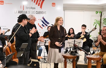Berta Rojas sonríe al micrófono, rodeada de músicos, en escenario decorado y con audiencia aplaudiendo.