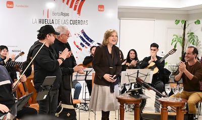 Berta Rojas sonríe al micrófono, rodeada de músicos, en escenario decorado y con audiencia aplaudiendo.