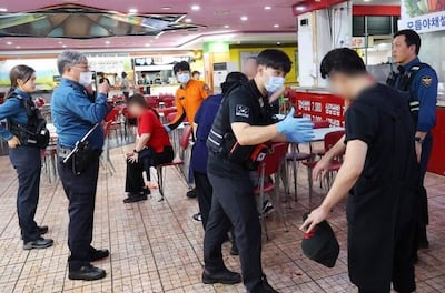Hombre en uniforme negro y guantes azules ayuda a persona herida en camiseta oscura, mientras otros observan en un ambiente de emergencia.