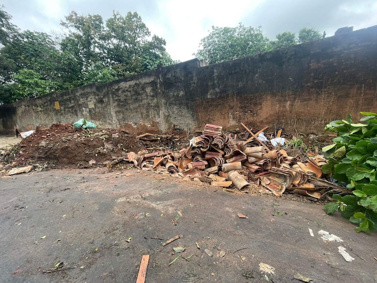 Montículo de escombros junto a un muro desgastado, con vegetación en el borde derecho de la imagen.