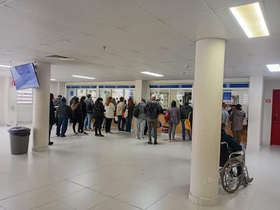 Grupo de pacientes, algunos con documentos, espera en el interior del IPS, uno en silla de ruedas observa.