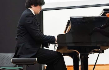 Juan Sebastián Giménez, con traje negro y camisa blanca, toca el piano en un auditorio, concentrado en su actuación.