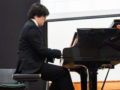 Juan Sebastián Giménez, con traje negro y camisa blanca, toca el piano en un auditorio, concentrado en su actuación.
