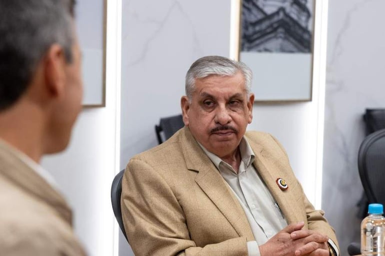Fretes con chaqueta beige y camisa clara escucha atentamente a Peña, en un entorno de reunión formal.