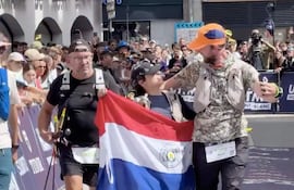 Hombre en camiseta negra y gafas interactúa con mujer que sostiene la bandera paraguaya, rodeados de una multitud celebrando.