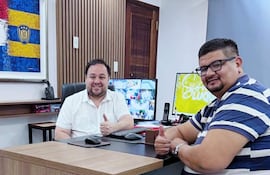 Mario Pineda sonríe con pulgar arriba junto a Hugui Farías también sonriendo, en oficina con computadoras de fondo.