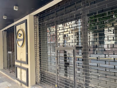 Fachada cerrada de 'Los Pinos', con reja metálica y cartel dorado en un entorno urbano vacío.