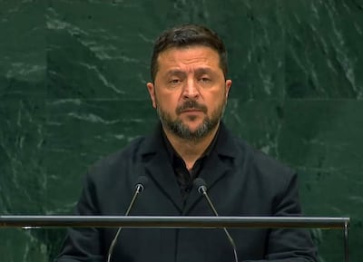 Zelenski, con chaqueta negra y barba, habla frente a un micrófono en un entorno formal de la ONU, de fondo verde oscuro.