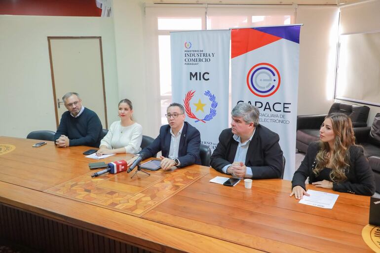 Romina Da Re y Gustavo Giménez sentados en mesa, rodeados de otros participantes en un salón de conferencias con pancartas institucionales.
