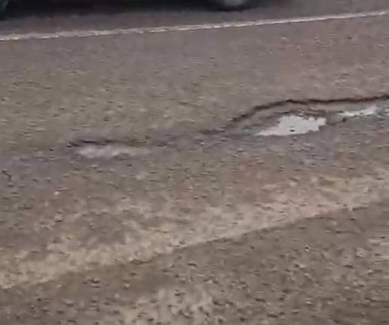 Tramo de la Ruta Bioceánica con baches profundos y agua acumulada, en un entorno urbano. No se observan personas.