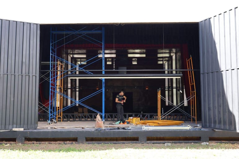Hombre de pie, enfocado en tareas de construcción, rodeado de andamiaje azul y amarillo en un auditorio en remodelación.