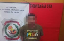 Hombre de 32 años en camiseta gris frente a cartel de la Comisaría 5ta de Policía Nacional en fondo naranja.