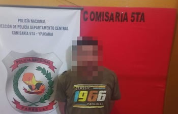 Hombre de 32 años en camiseta gris frente a cartel de la Comisaría 5ta de Policía Nacional en fondo naranja.