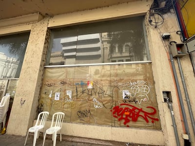Entorno urbano deteriorado con sillas apiladas, graffitis en una pared y posters adheridos a una lona.