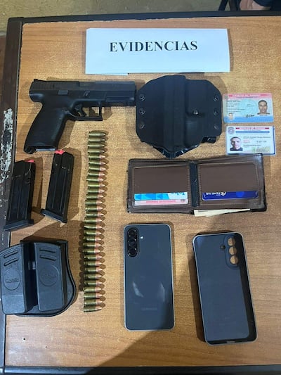 Escritorio con una pistola negra, cargadores y documentos de identidad en un entorno policial.