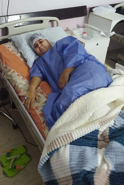 María Ojeda en bata de hospital azul, acostada en una cama con expresión neutra y vía intravenosa en su brazo.
