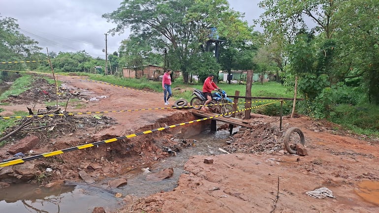 Hombre en chaqueta roja sobre una estructura improvisada; mujer en camiseta rosa observa la situación en un camino rural con vegetación.