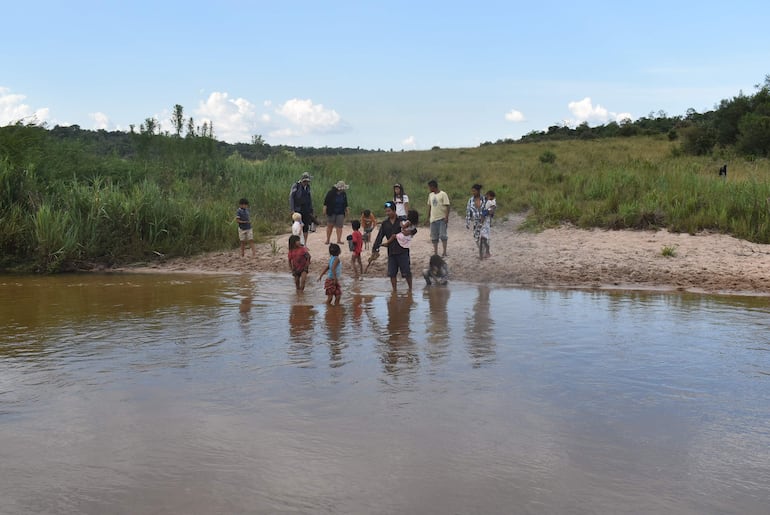 Grupo de personas en ropa ligera interactuando cerca del arroyo Tapiracuai, niños juegan mientras un hombre sostiene una rama.