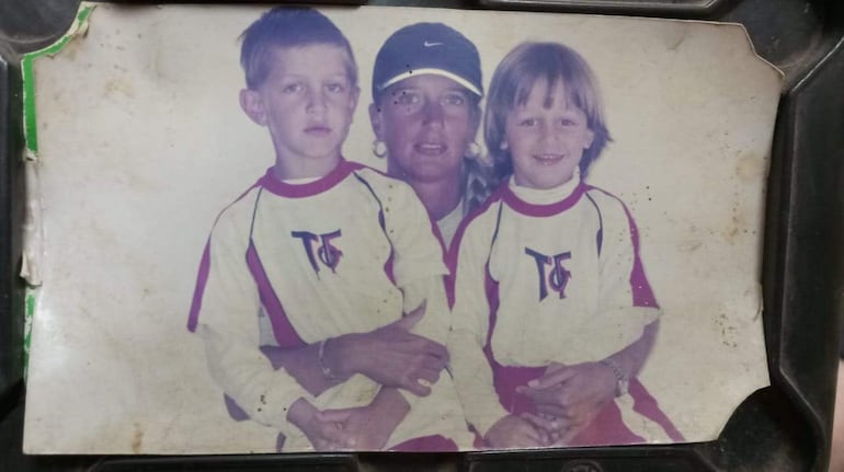 Romina Fonda en gorra negra sonríe entre Matías y Lucas, ambos con camisetas de fútbol, en un ambiente familiar interior.