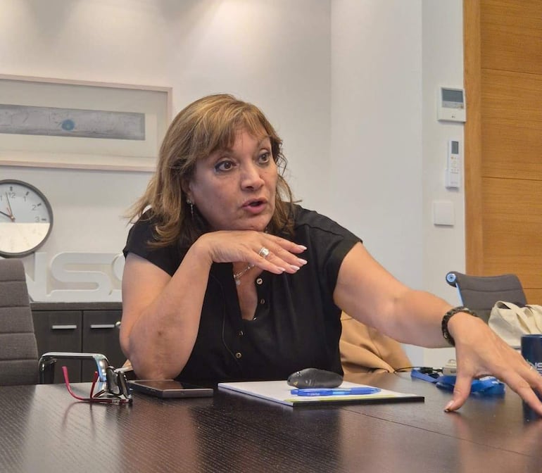 Orna Mizrahi, con blusa negra y cabello castaño, gesticula en una mesa con cuaderno y gafas, en un ambiente de oficina.