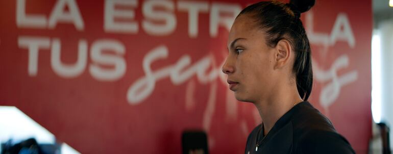Claudia Martínez, en perfil y con coleta alta, viste ropa deportiva oscura mientras reflexiona en un entorno de entrenamiento.