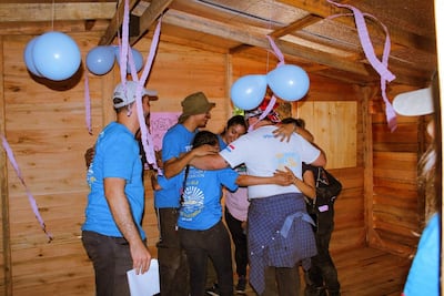 Siete personas con camisetas azules se abrazan en un ambiente festivo decorado con globos azules y cintas de papel.