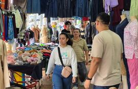 Multitud de compradores en un mercado exterior, con una mujer joven en abrigo blanco y hombres observando alrededor.