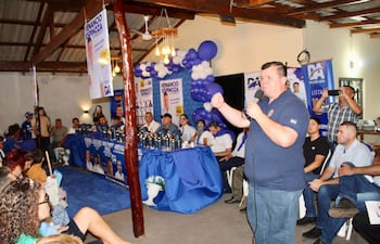 Dionisio Amarilla habla enérgicamente con micrófono, mientras la audiencia escucha atenta rodeada de globos azules y blancos.