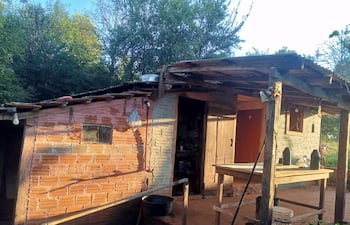 Estructura rústica de vivienda con vegetación, mesa de madera y utensilios visibles en un entorno exterior tranquilo.
