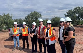 Grupo de ocho personas, en su mayoría mujeres, con cascos de seguridad y chalecos de alta visibilidad, discuten en un terreno abierto.