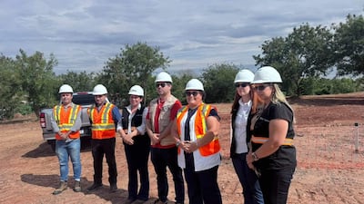 Grupo de ocho personas, en su mayoría mujeres, con cascos de seguridad y chalecos de alta visibilidad, discuten en un terreno abierto.