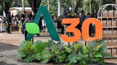 Multitud en evento al aire libre con decoraciones en verde y naranja, personas en ropa casual y formal.