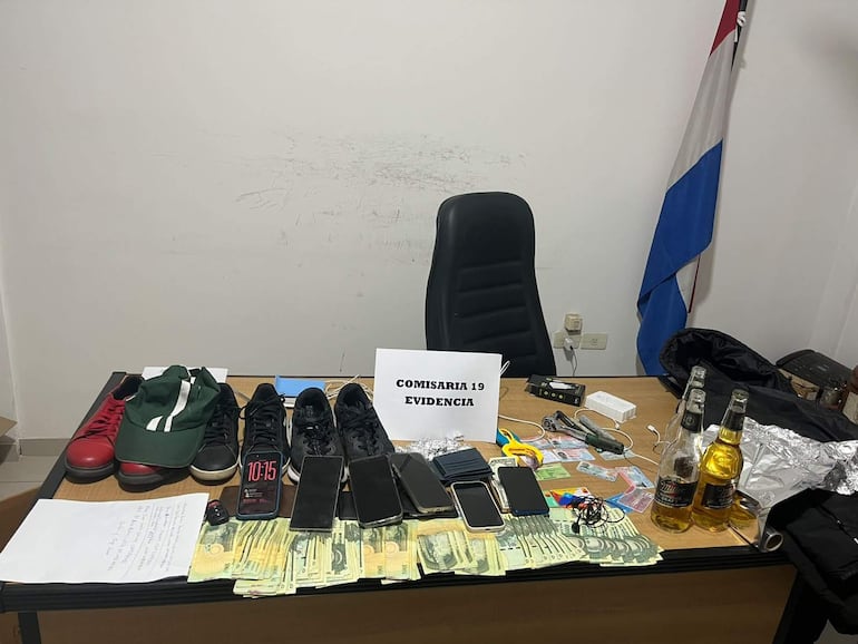 Mesa con evidencia en Comisaría 19: zapatos rojos, teléfonos y dinero apilado, sin personas visibles.
