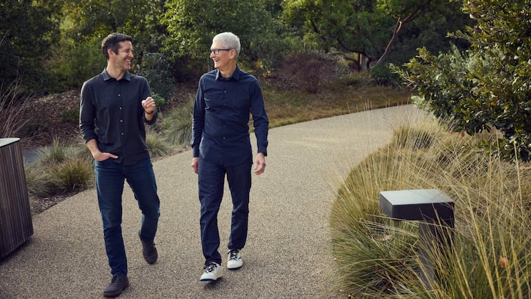 John Ternus y Tim Cook sonríen mientras caminan, ambos vestidos elegantemente en un ambiente de evento tecnológico.
