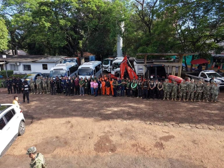 Grupo de 70 personas en uniformes de seguridad y ropa de trabajo, con excavadora y vehículos en un entorno exterior.