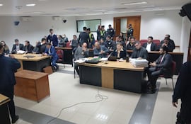 Hombres y mujeres en sala judicial, atentos y tomando notas, en ambiente tenso durante la suspensión del juicio.