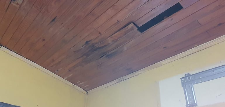 Techo de la Escuela Onorio Takachi con estructura de madera dañada, manchas oscuras y paredes amarillas que indican abandono.