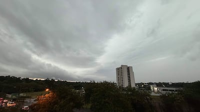 Edificio alto a la derecha con cielo nublado y árboles a la izquierda en un ambiente urbano antes de la lluvia.