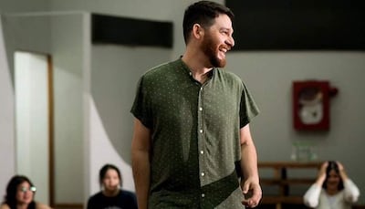 Héctor Lozzca sonríe, vistiendo una camisa verde con puntos, mientras habla en un salón con audiencia visible.