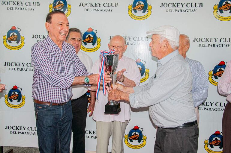 Juan Carlos Aveiro (i) recibe la copa de manos de Evelio Montebruno, por la victoria de Criscraft que consagró mejor potrillo del 2023.