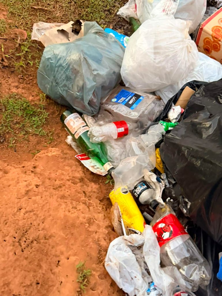 Residuos plásticos y botellas abandonadas en un terreno sin personas visibles, reflejando una problemática ambiental.