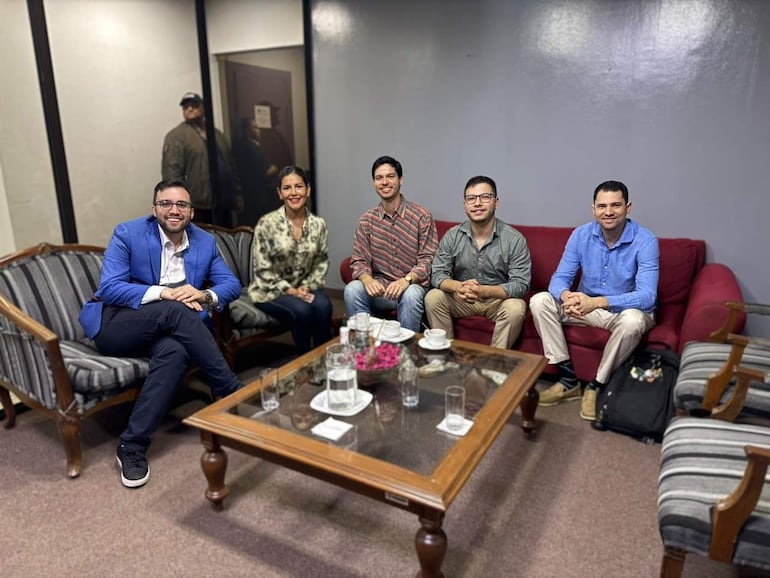Sole Núñez en blusa clara y varios hombres con camisas coloridas, todos sonriendo en un ambiente de reunión.