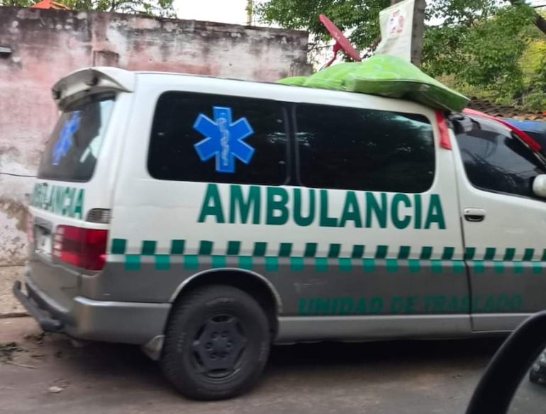 Parte trasera de una ambulancia con la inscripción 'UNIDAD DE TRASLADO' y cruz azul, estacionada en una calle con vegetación.