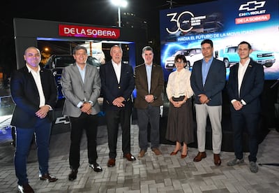 Álvaro Espínola y Augusto Wagner sonríen en evento formal, rodeados de otras cinco personas, con fondo iluminado de Chevrolet.