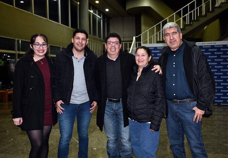 Cinco personas sonriendo en el Teatro Lírico, con abrigos oscuros y blusa roja, posando para la foto en un ambiente iluminado.