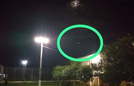 La imagen muestra un entorno nocturno, probablemente al aire libre. No hay personas visibles en la escena. Se aprecian varias fuentes de luz, incluyendo dos faroles que iluminan la área cercana y sugieren que es un espacio utilizado para actividades, posiblemente un campo deportivo.
En la parte superior, hay una luna parcialmente oculta por nubes, y en el área marcada, se puede ver un objeto luminoso, que podría ser un planeta o una estrella brillante, pero no se puede identificar con certeza su naturaleza.
No se reconocen elementos visuales relacionados con un equipo de fútbol, como camisetas o escudos, y no hay monumentos o lugares icónicos identificables en la imagen. La ambientación parece ser serena y tranquila, sin acciones específicas en curso. No hay texto visible ni elementos adicionales de contexto noticioso.