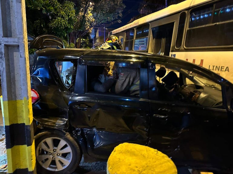Un vehículo negro dañado con una persona dentro, visible con la mano en su rostro en un entorno urbano nocturno.