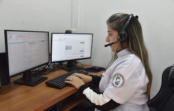 Mujer con auriculares y camisa blanca en escritorio, concentrada en monitores en una oficina del IPS.