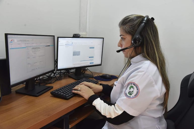 Mujer con auriculares y camisa blanca en escritorio, concentrada en monitores en una oficina del IPS.