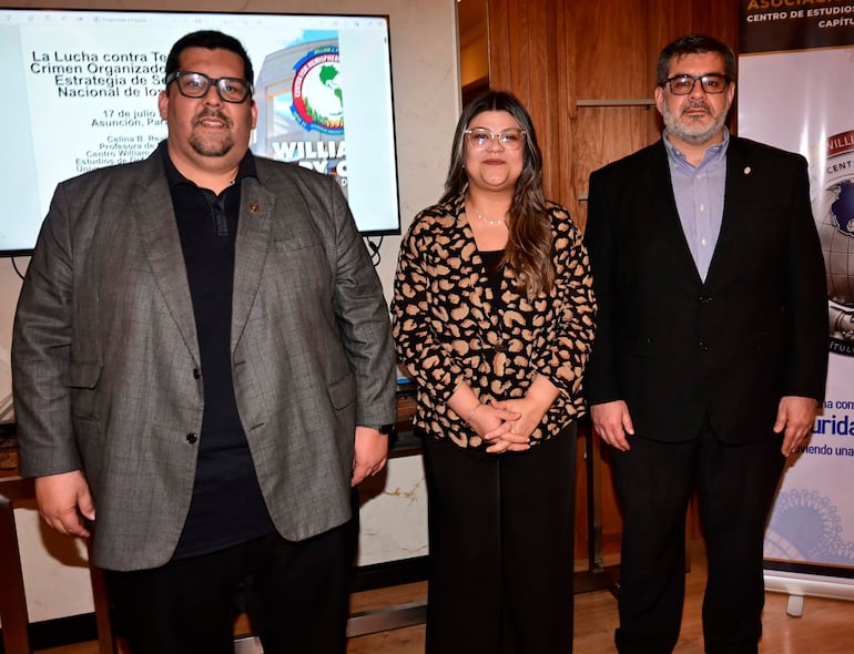 María Isabel Rodríguez en cena de egresados, con abrigo y expresión feliz, posando junto a dos hombres en un entorno formal.